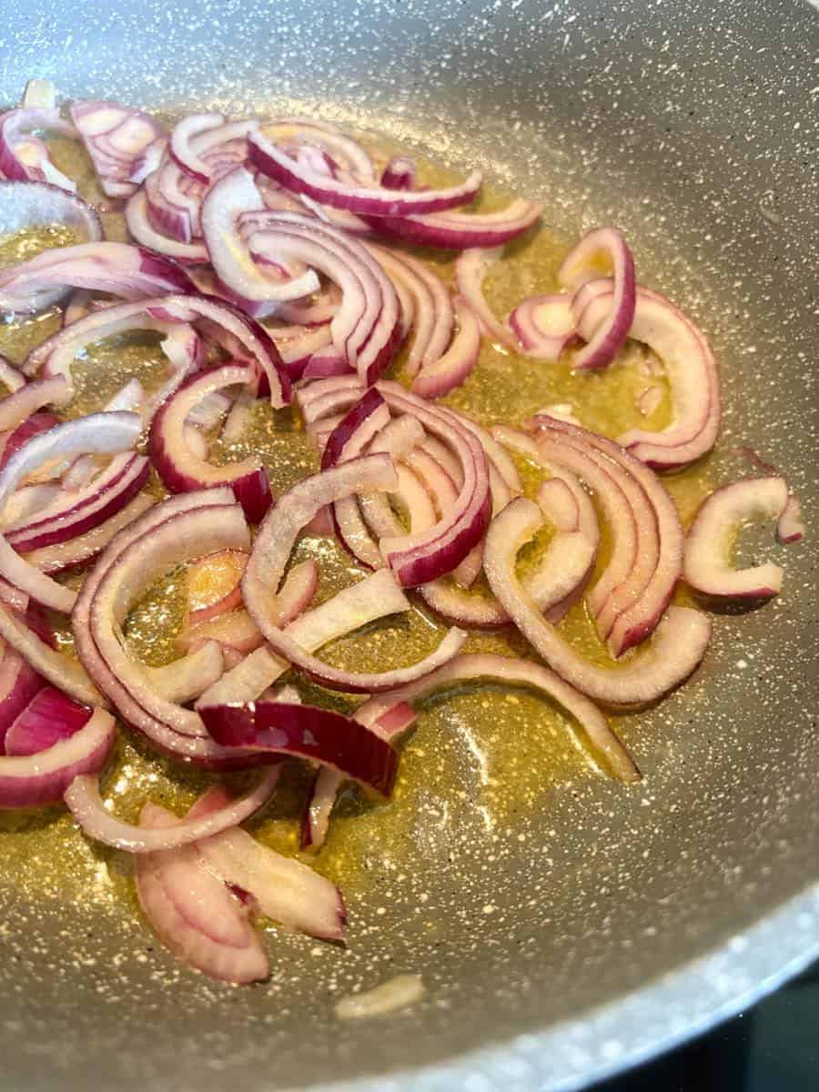 Sliced red onions frying in butter in a grey pan.