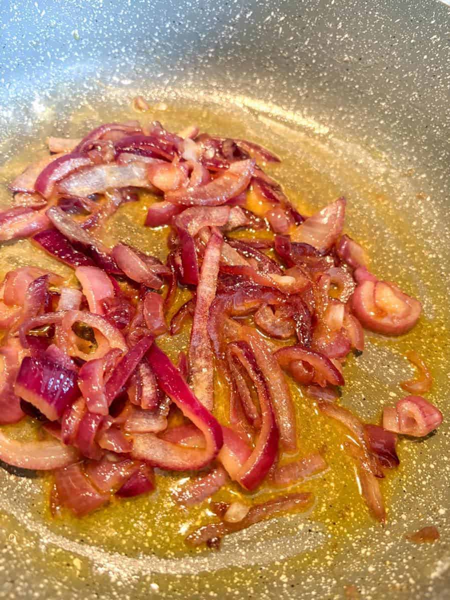 Sliced red onions cooking in melted butter in a grey saucepan.