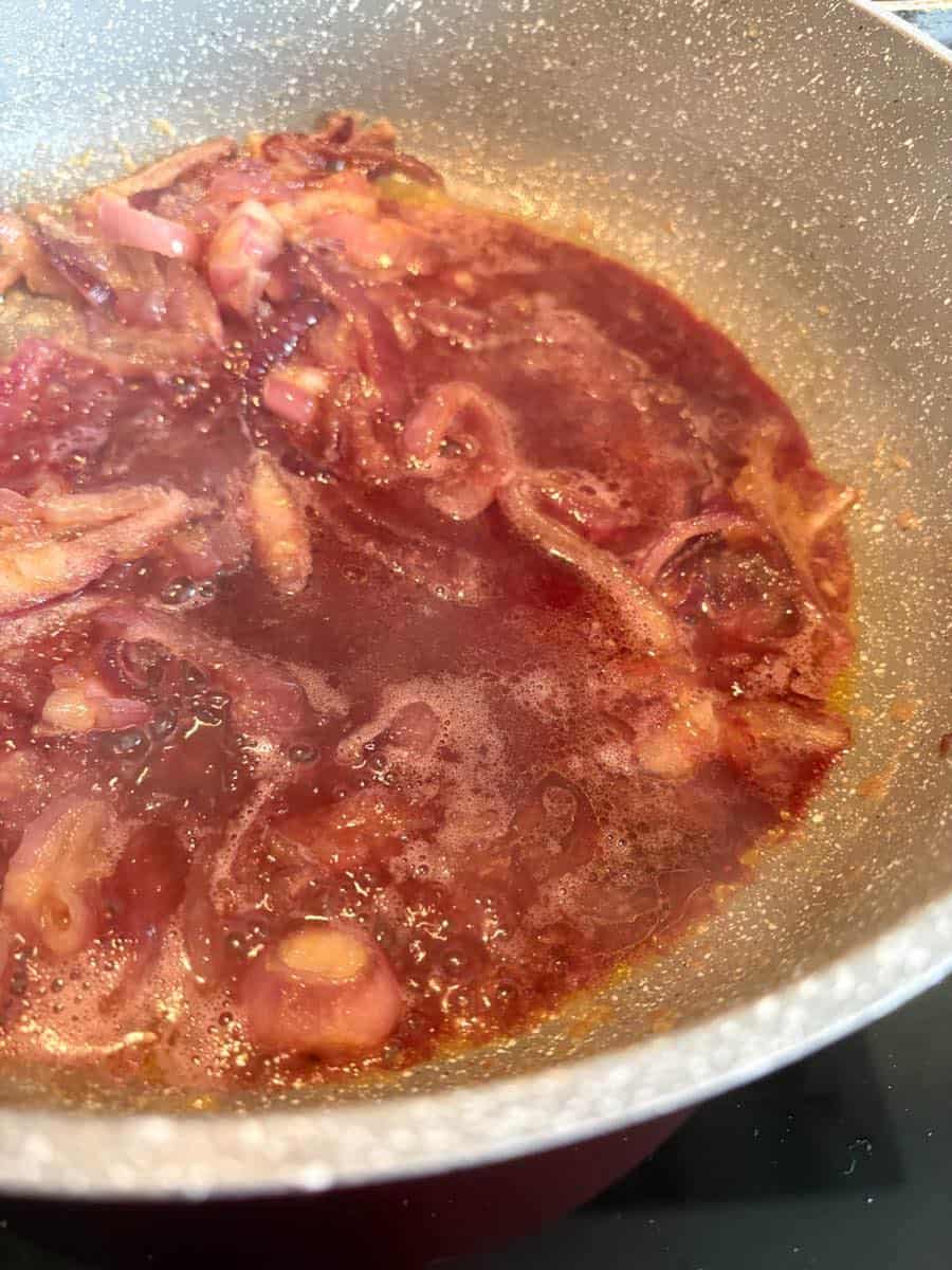 Cooked sliced red onions and red wine simmering in a grey saucepan.