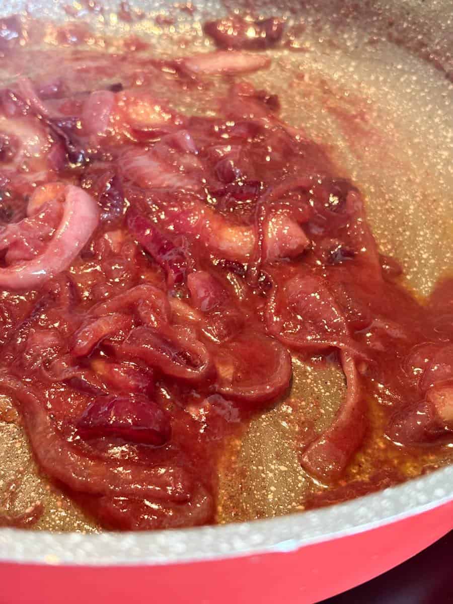 Cooked sliced red onions in a red and grey saucepan.