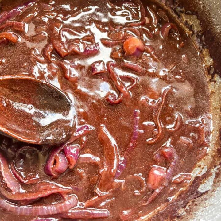 A grey pan of red onion gravy with a wooden spoon.
