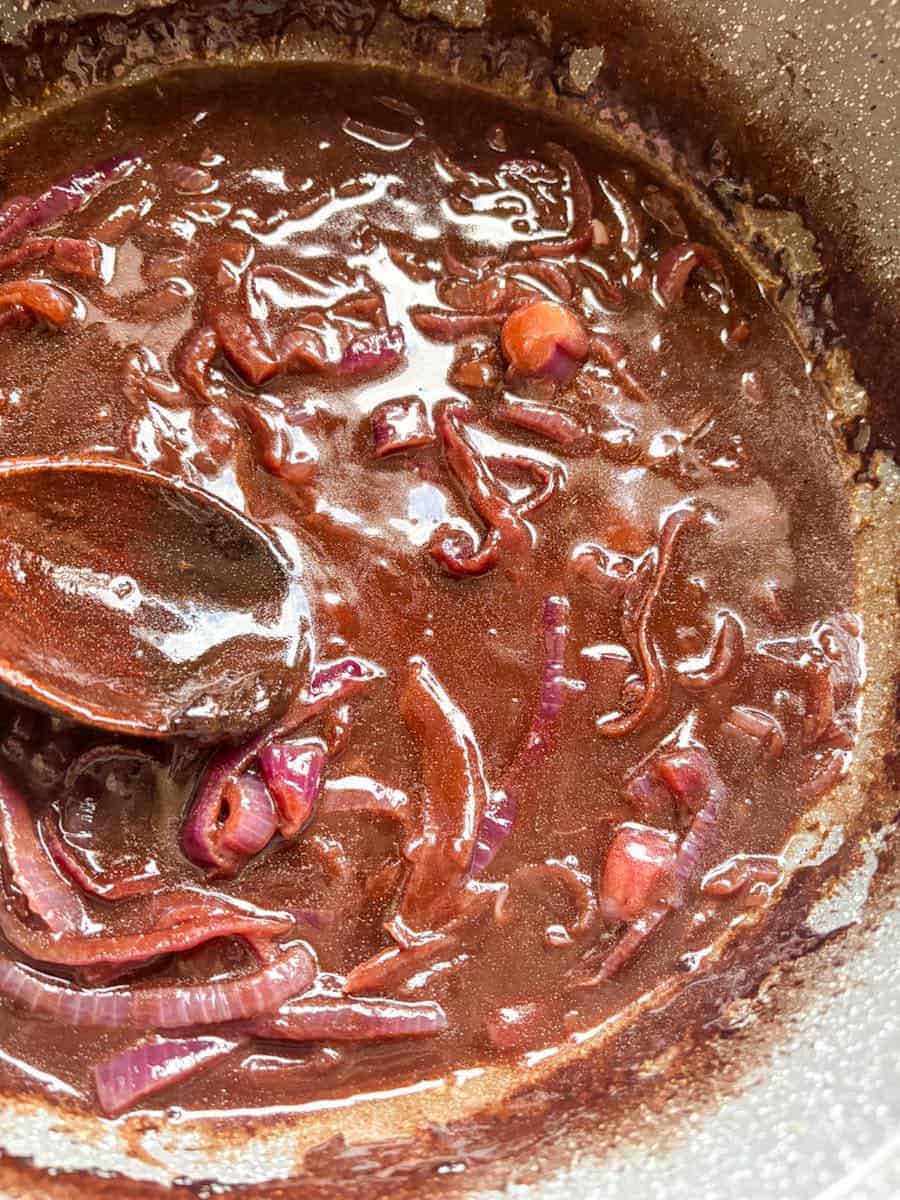 A grey pan of red onion gravy with a wooden spoon.