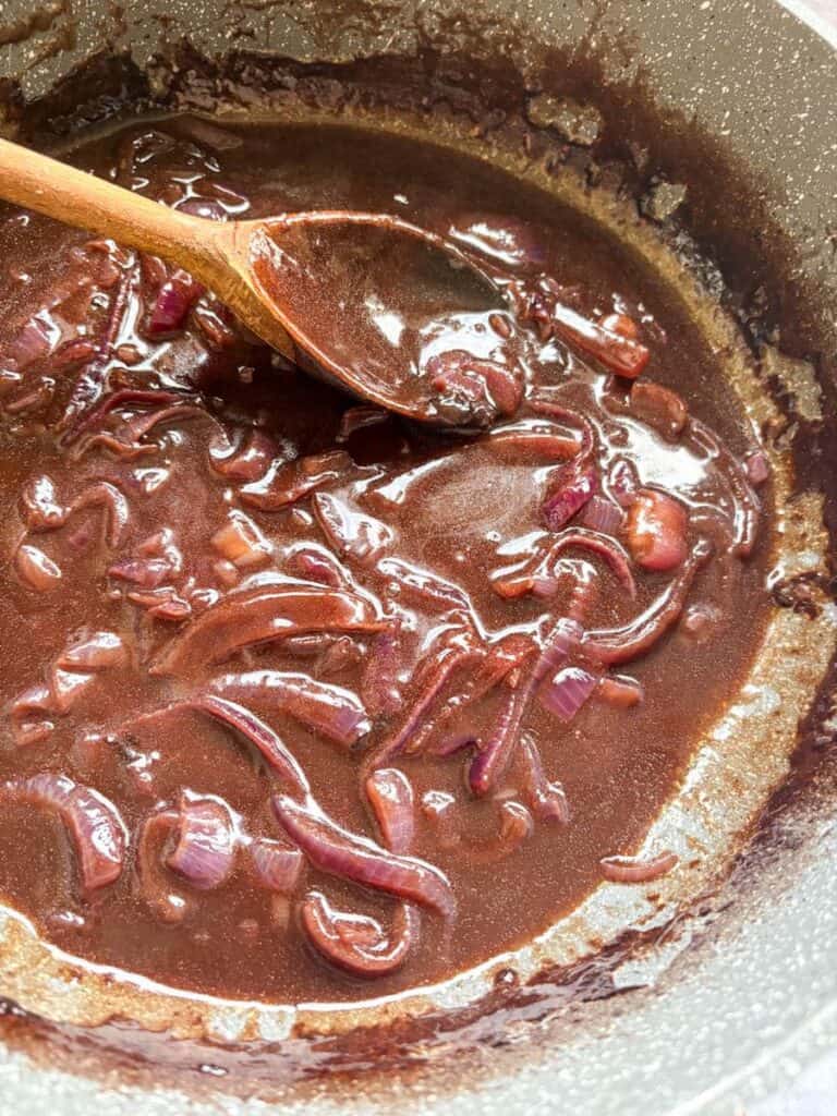 A grey pan of red onion gravy with a wooden spoon.