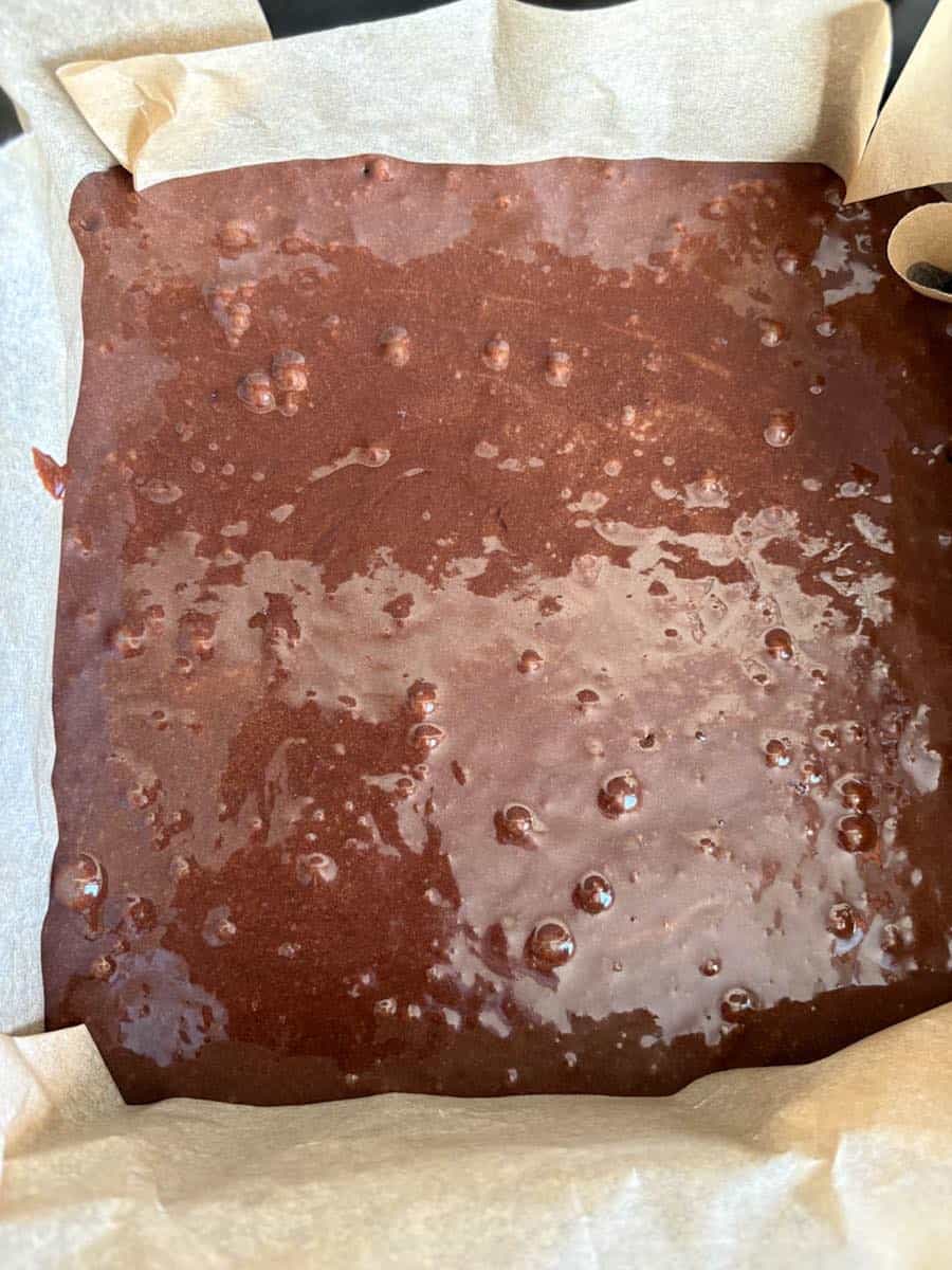 brownie batter poured into a square cake tin lined with baking paper.