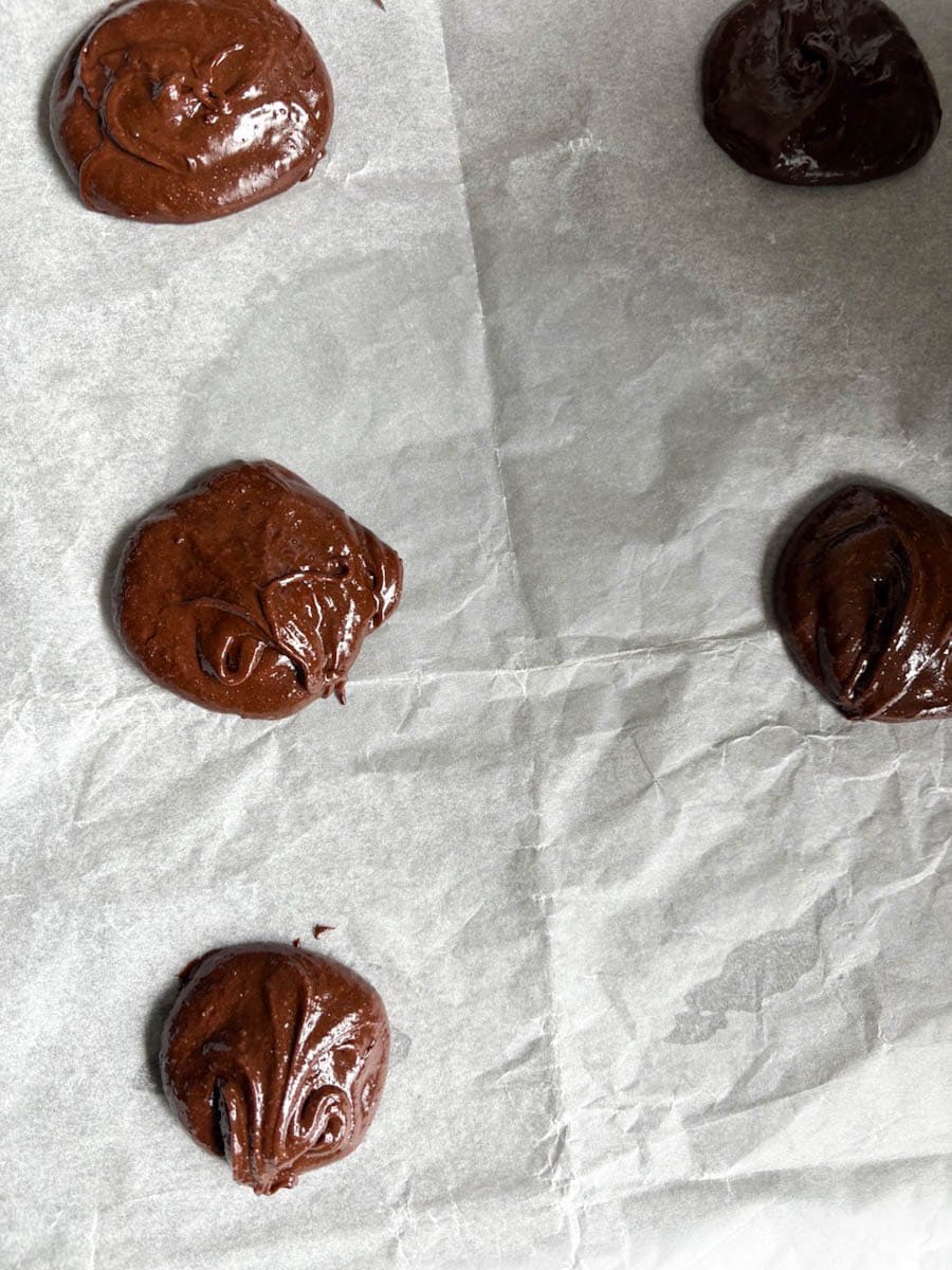 Five unbaked chocolate cookies on a lined baking tray.