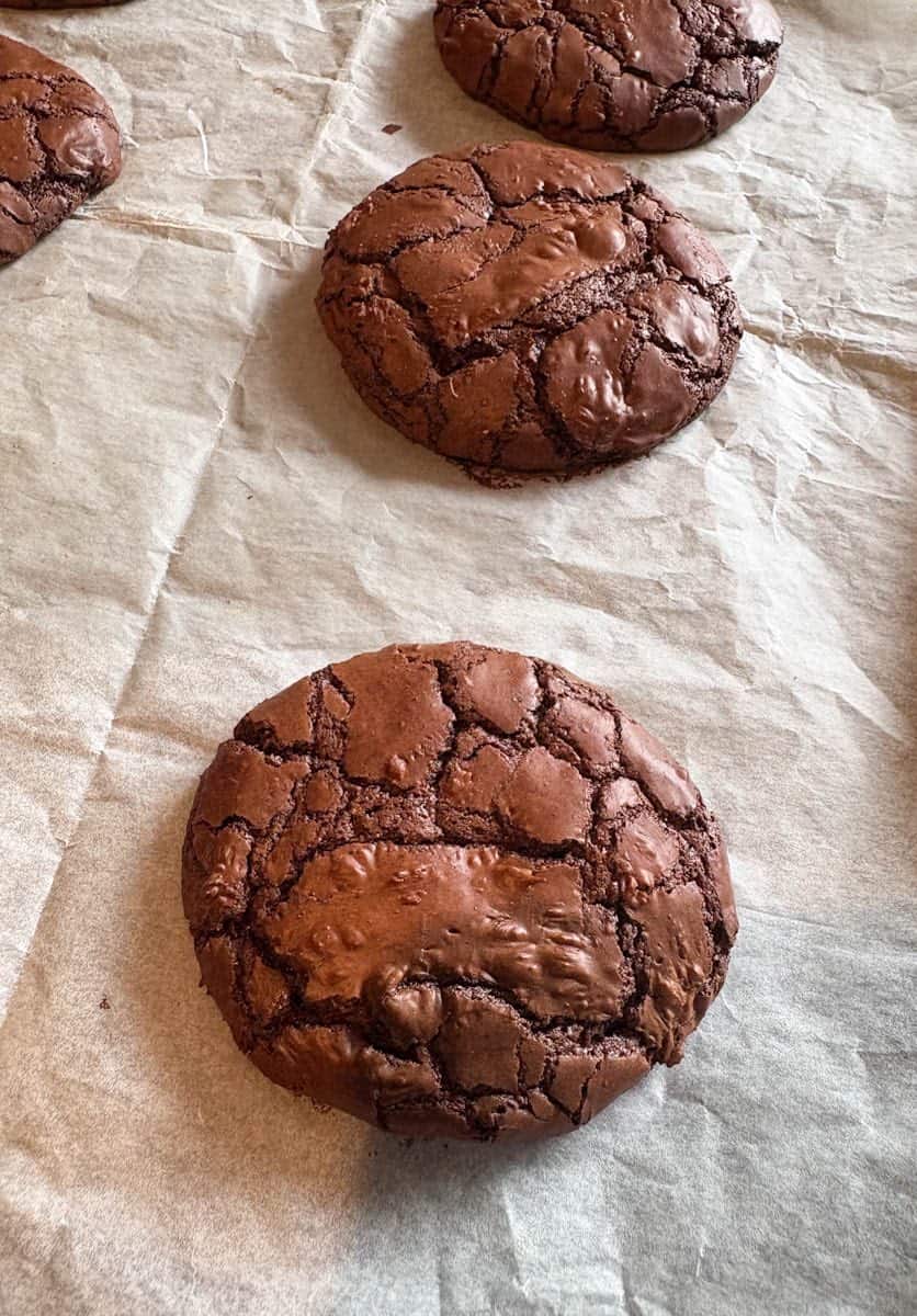 Three chocolate brownie cookies on a lined baking tray.