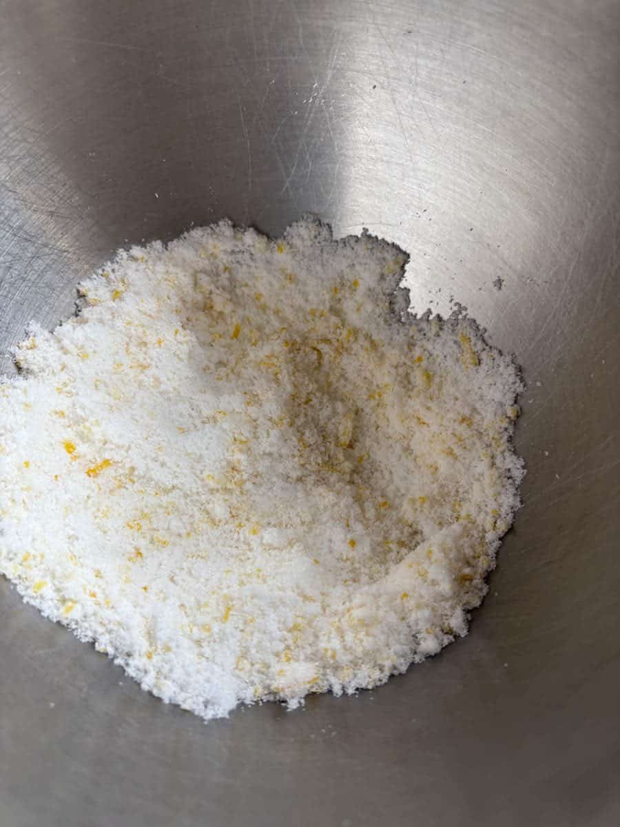 A silver bowl of white sugar with finely grated lemon zest.
