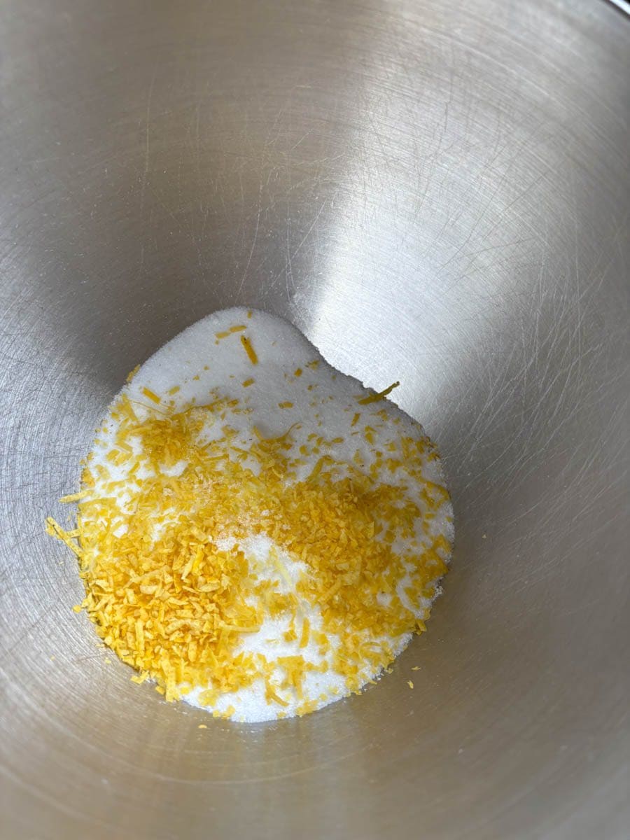 A silver bowl of white sugar and grated lemon zest.