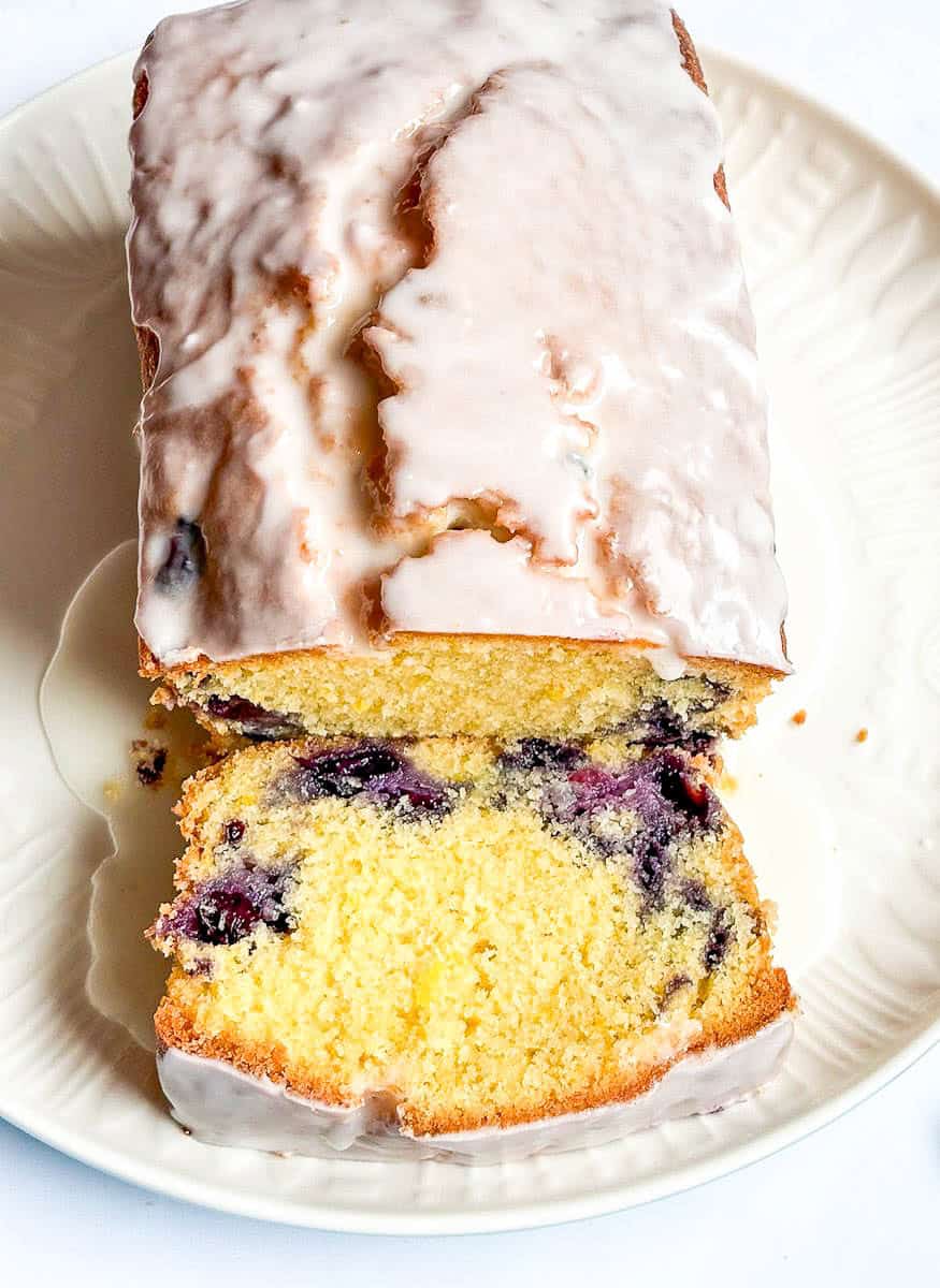 A sliced lemon and blueberry loaf cake covered in white icing on a white plate.