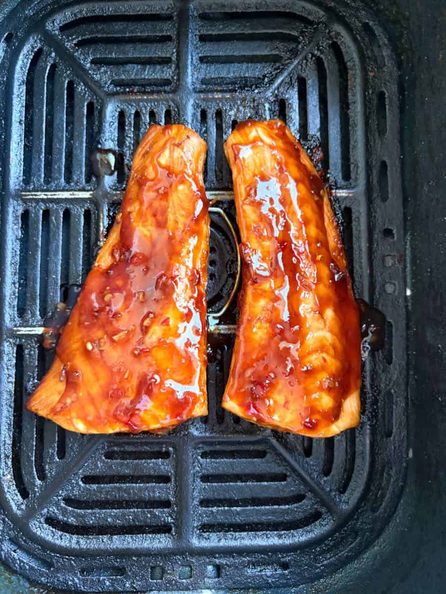 Two partially cooked salmon fillets covered in sweet chilli marinade inside an air fryer basket.