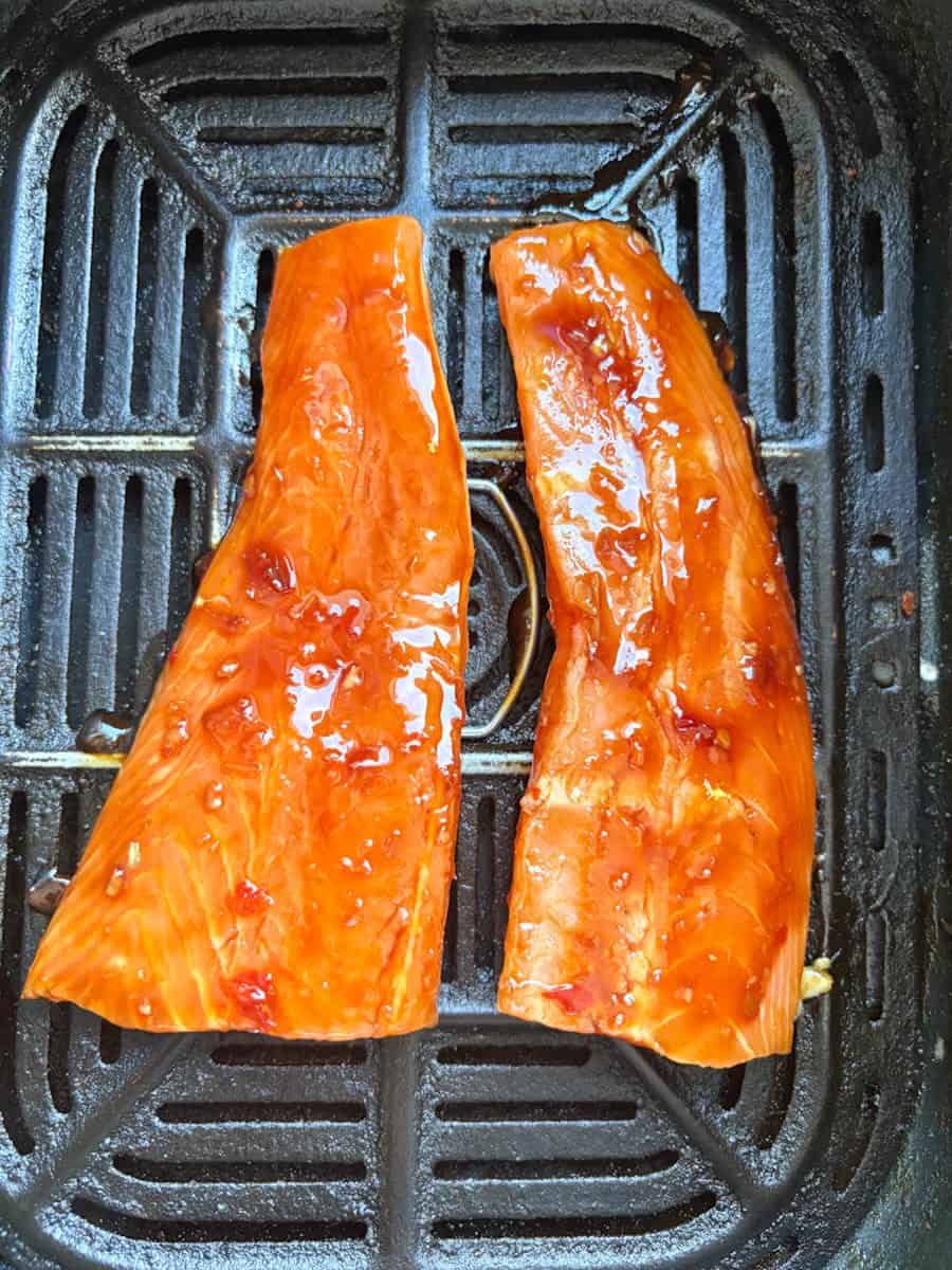 Two raw salmon fillets covered in sweet chilli marinade inside an air fryer.