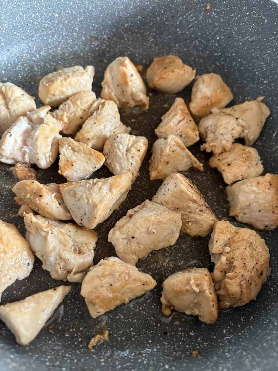 Chicken pieces cooking in a grey pan.