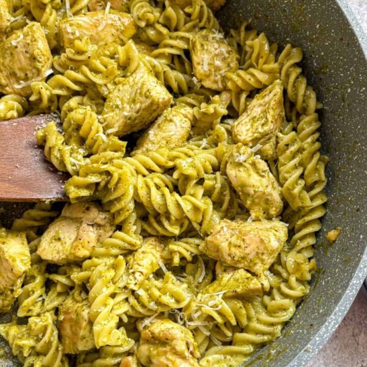 A large grey pan of chicken pesto pasta with a wooden spoon.