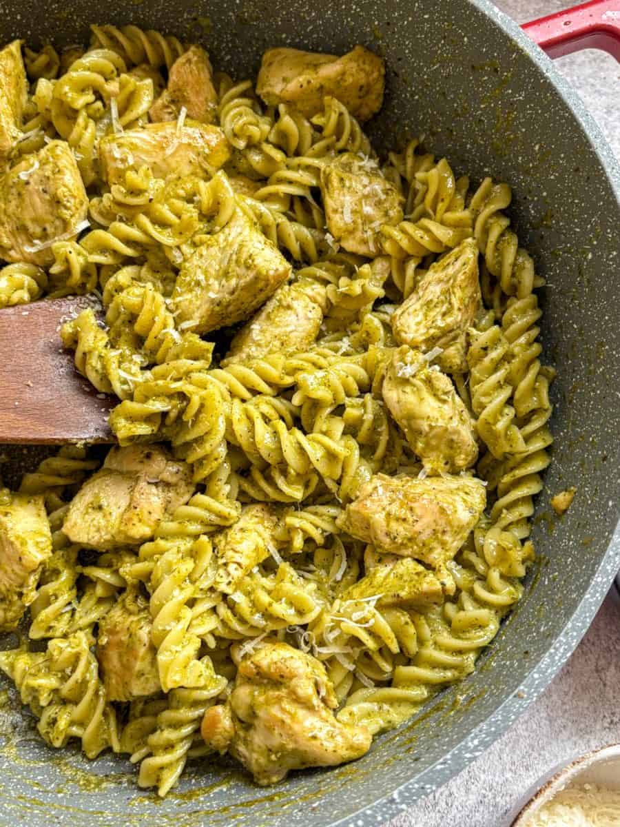 A large grey pan of chicken pesto pasta with a wooden spoon.