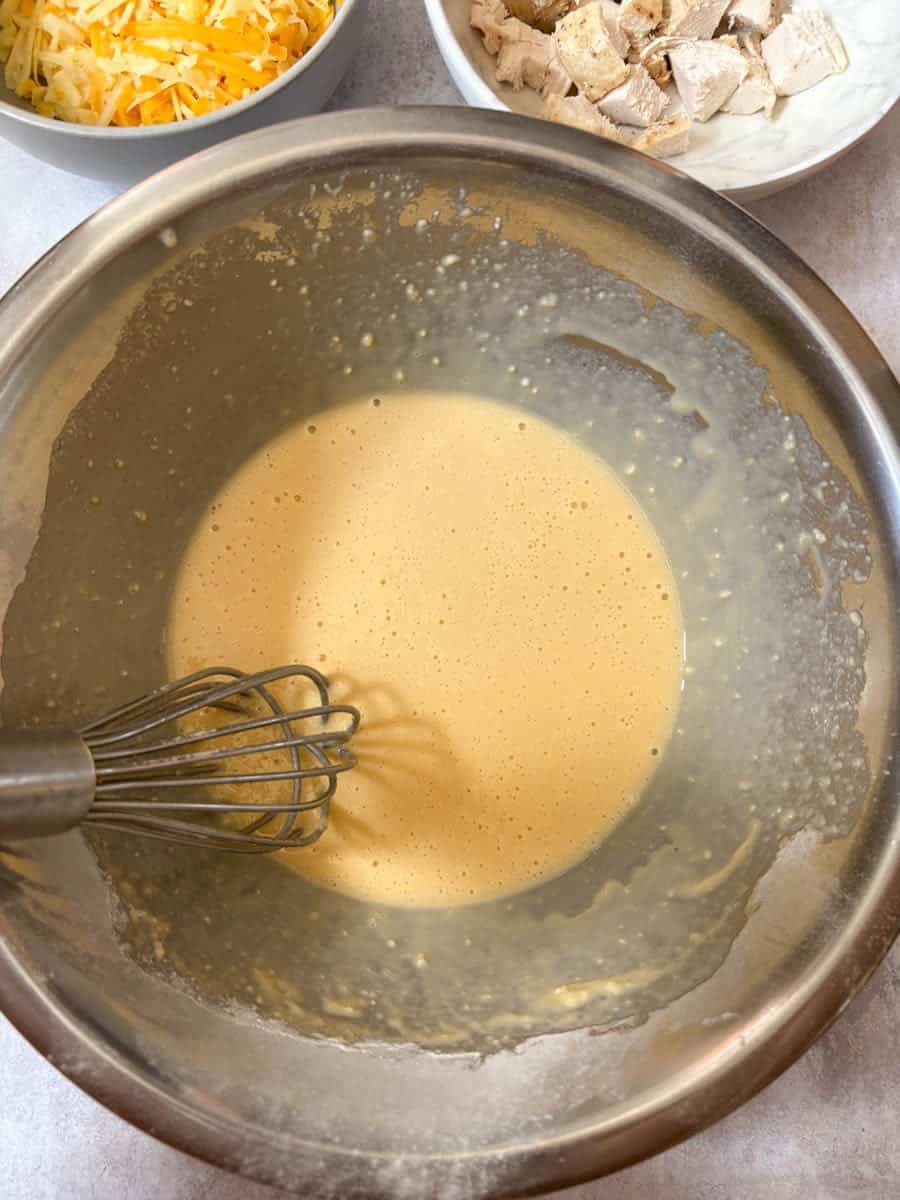 A large silver bowl of whisked eggs and milk with a silver whisk.
