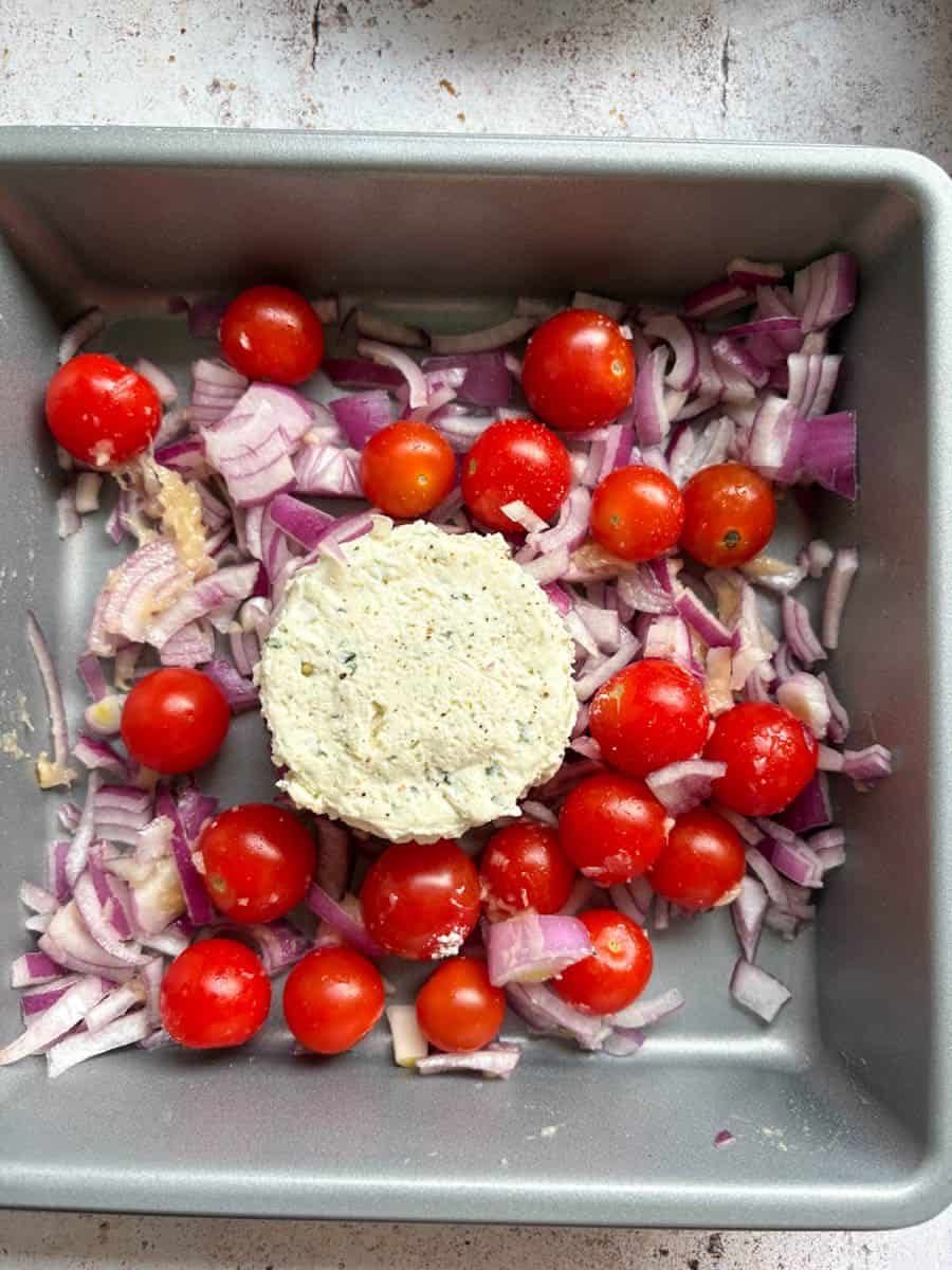 A silver tin with cherry tomatoes, diced red onion and a wheel of Boursin cheese.