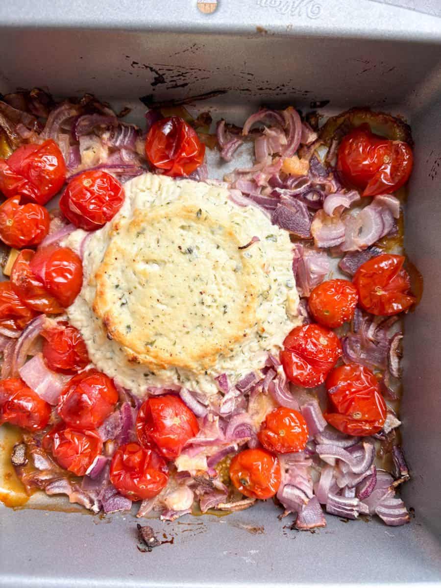 A silver pan of baked Boursin cheese, chopped red onion and cherry tomatoes.