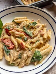 A blue and white bowl of Penne pasta with Boursin cheese, cherry tomatoes, fresh spinach and basil.