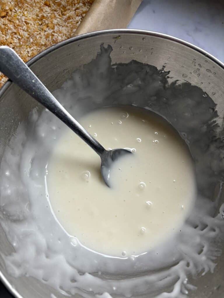 A silver bowl of lemon icing with a silver spoon.