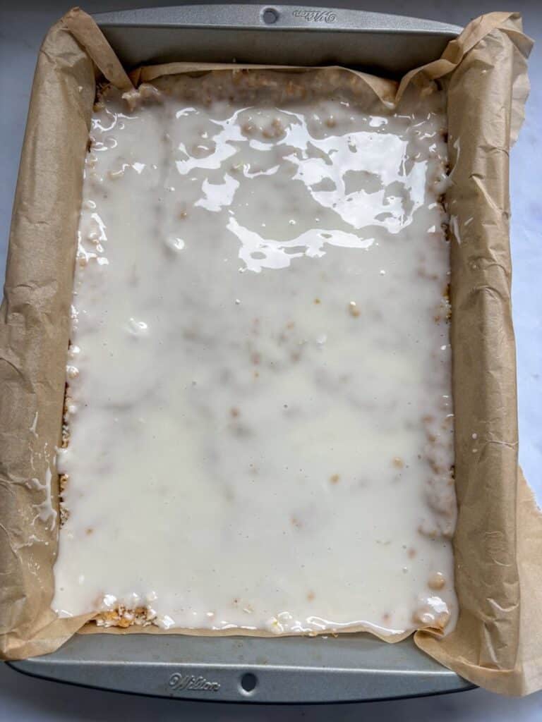 A lemon and coconut traybake with lemon glaze icing in a lined rectangular baking tin.