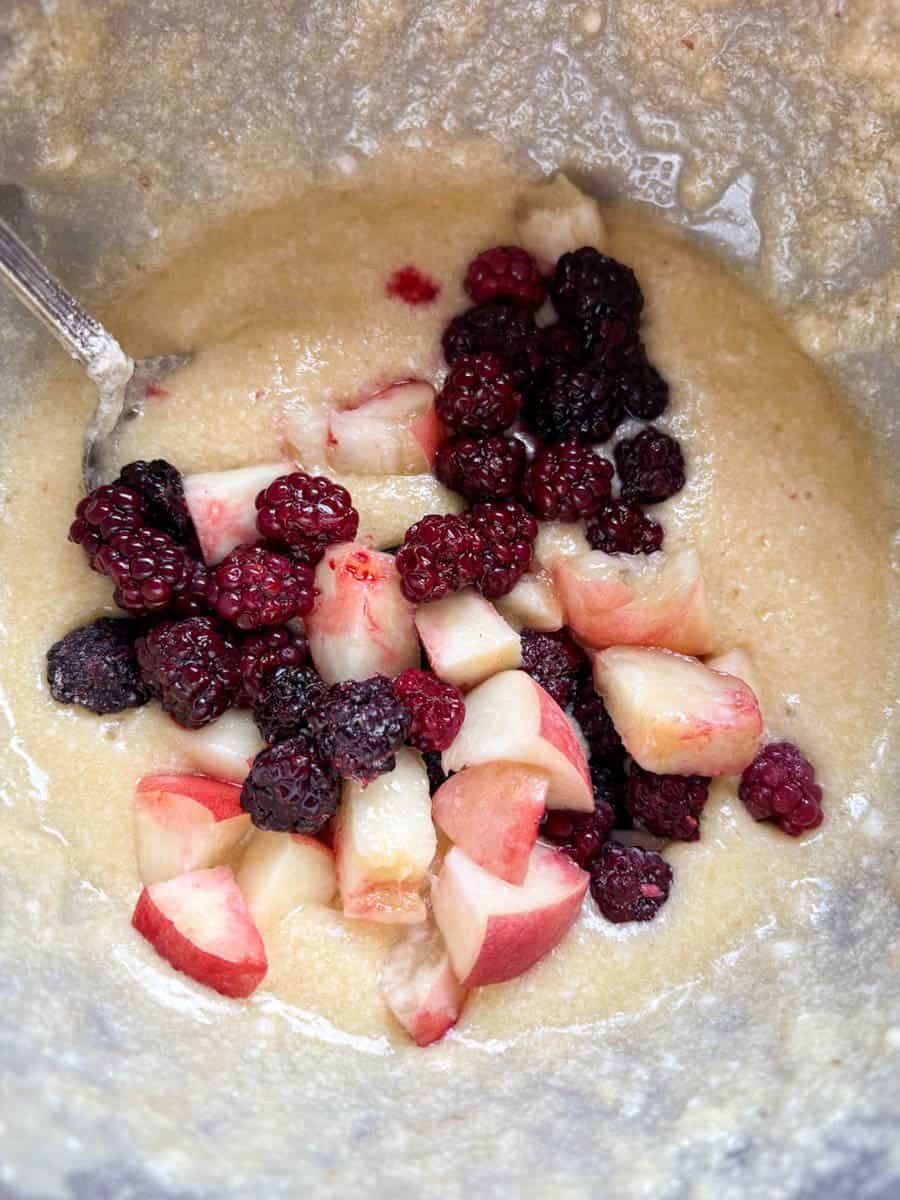Blackberries and chopped peaches being folded into cake batter.