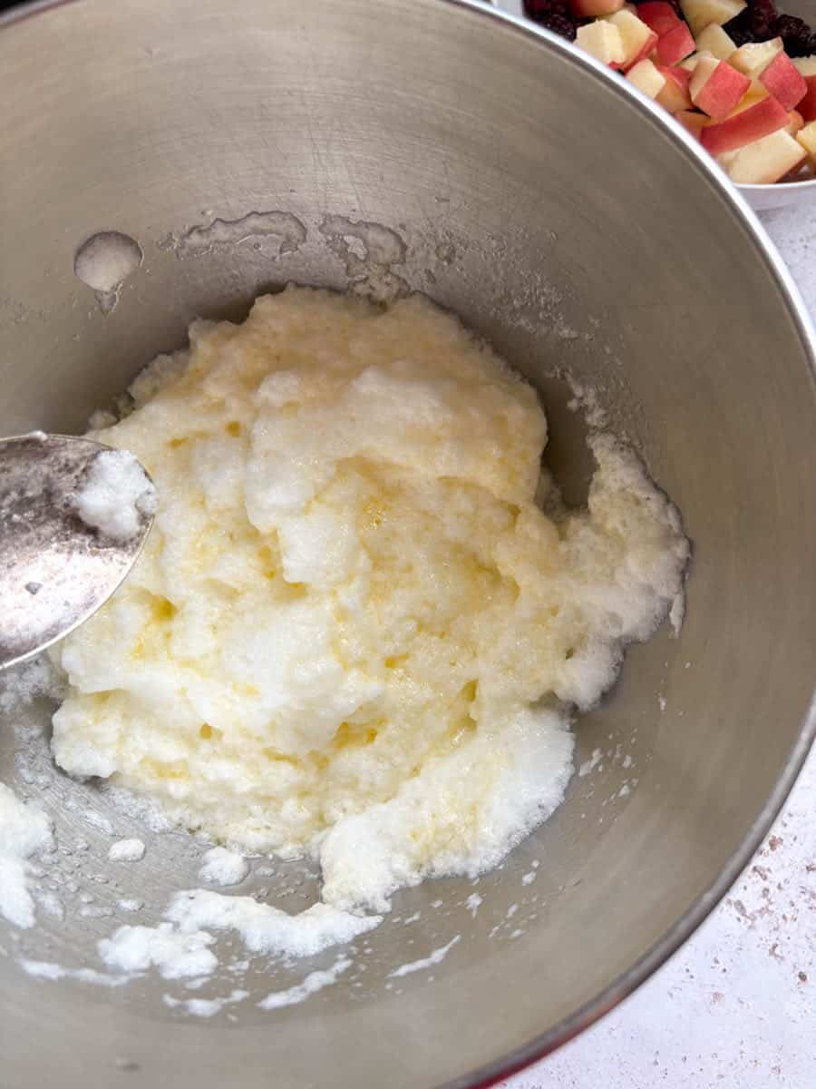 A large silver bowl of whisked egg whites and melted butter. A small bowl of chopped peaches and blackberries can be partially seen.