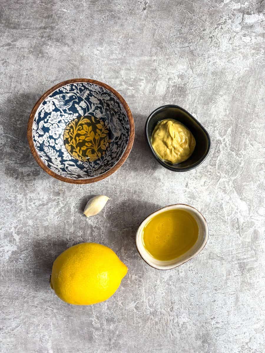 Bowls of mustard, honey, olive oil, a clove of garlic and a lemon.