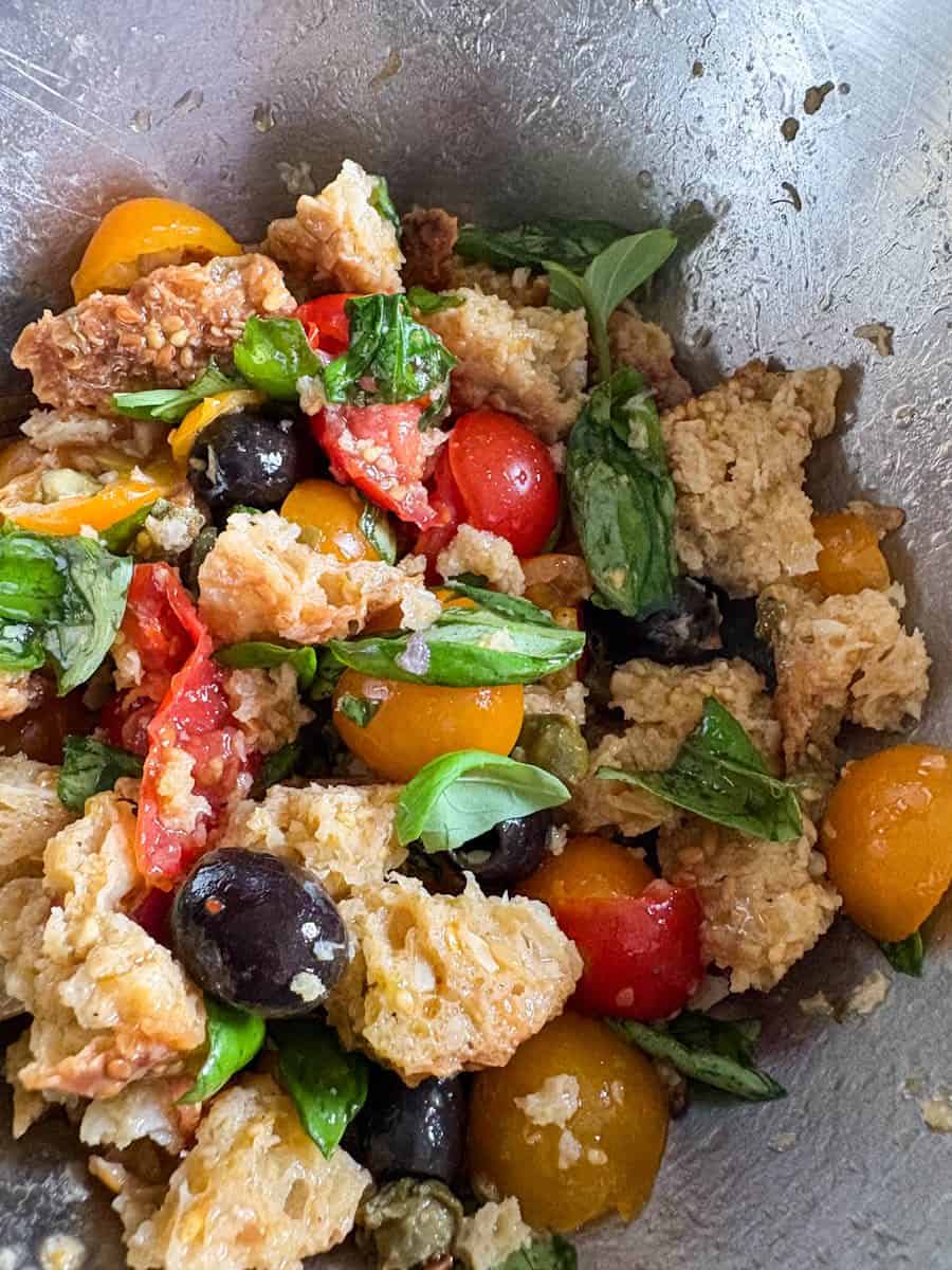 A Panzanella salad with black olives, capers, tomatoes and fresh basil in a silver bowl.